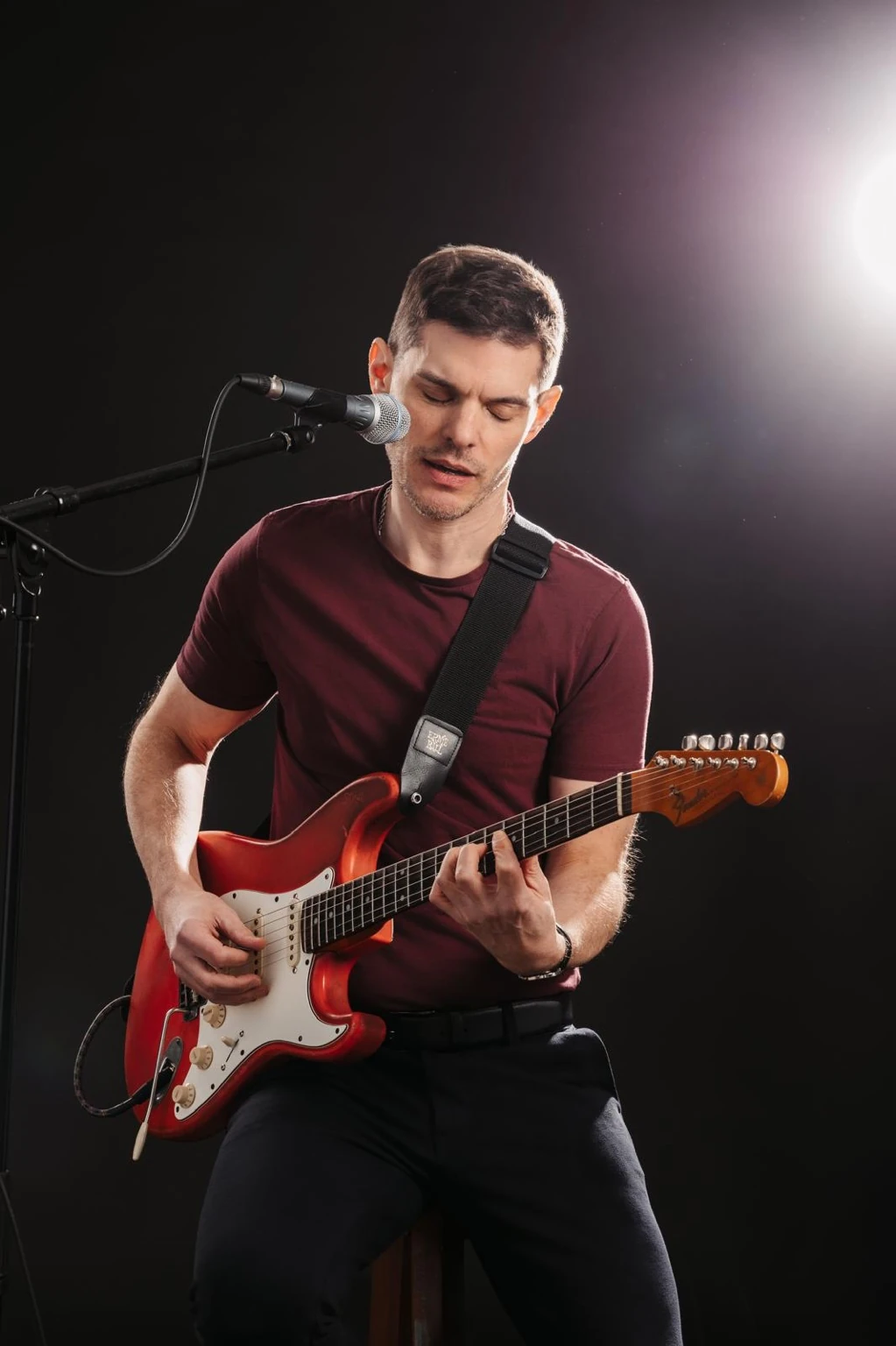George Kramer spielt konzentriert eine rote Stratocaster vor schwarzem Hintergrund